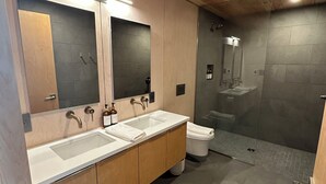 A modern bathroom with wooden ceiling, a double sink vanity, a toilet, and a glass-enclosed shower area.
