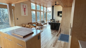 A spacious kitchen with wooden cabinets, a large island, and a view of the forest through large windows.