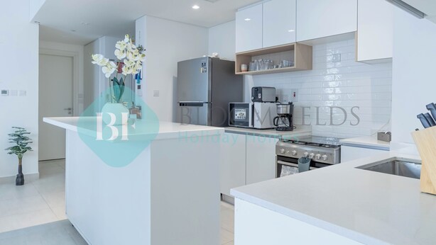 A modern kitchen with white cabinetry, a built-in oven, a microwave, and a coffee maker. - Bloomfields Metropolitan 3BR In Bridges (Abu Dhabi)