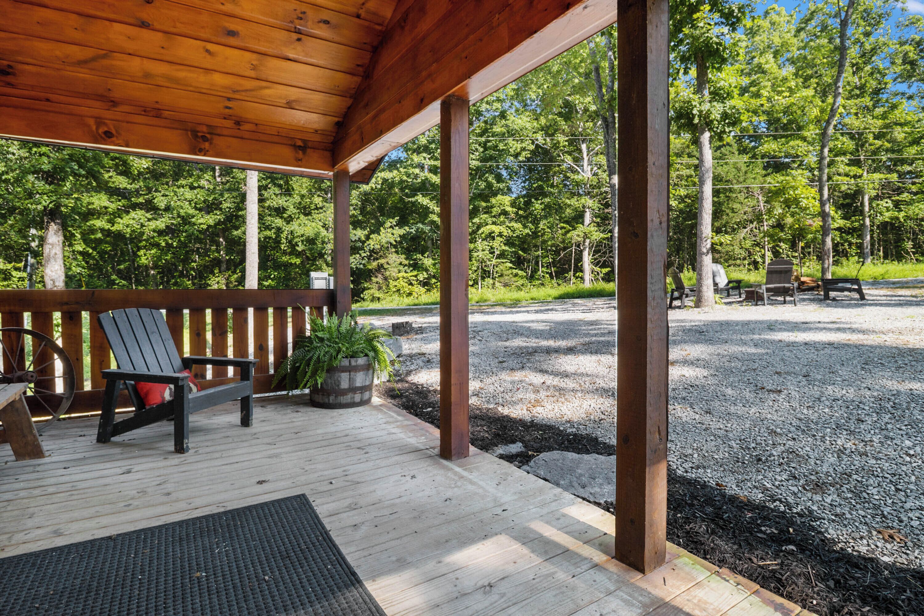 Un patio in legno coperto con una panchina e un fioriera, circondato da ghiaia e alberi.