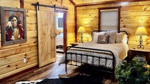 A wooden cabin bedroom with a bed, two bedside lamps, a window, and a painting on the wall. - ๐๐ข๐ ๐๐จ๐ฎ๐ญ๐ก ๐
๐จ๐ซ๐ค Retreat! Excellent LocationโขPrivateโขWIFI, 75โ TV, Horses Welcome! (Strunk)