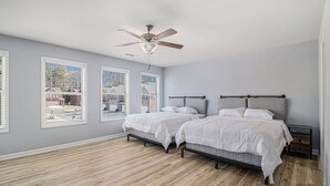A bedroom with two beds, a ceiling fan, and large windows.