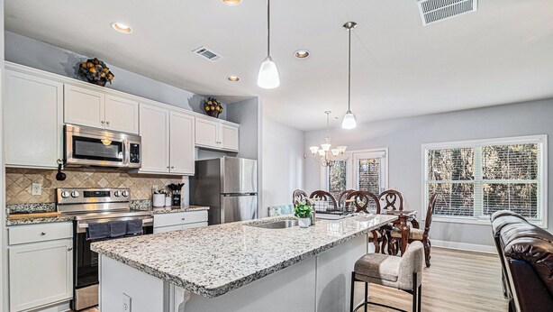 A modern kitchen with white cabinetry, stainless steel appliances, a granite island, and a dining area with wooden chairs and a bench.