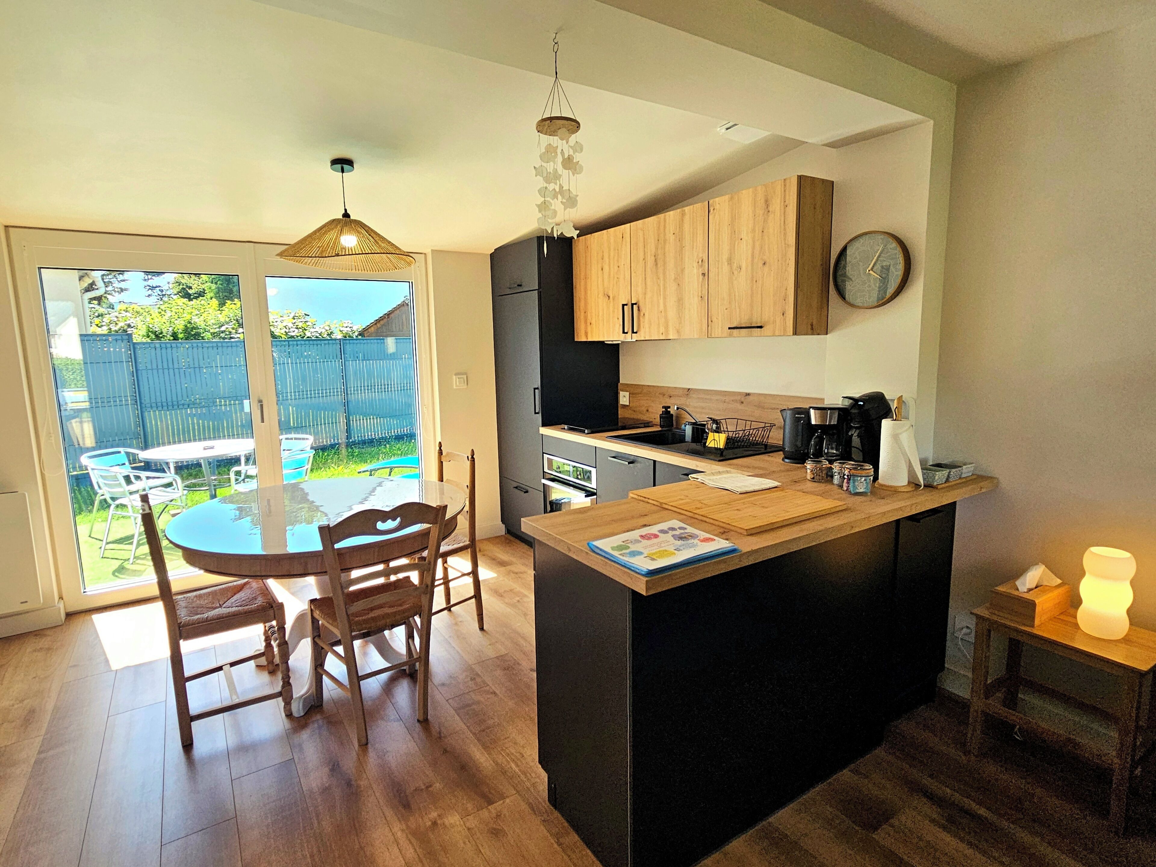 A modern kitchen with wooden cabinets, a black refrigerator, and a dining area with a glass table and chairs.