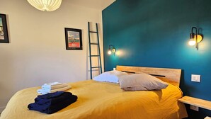 En seng med et trægavl, en stige, en vægmonteret lampe og et billede i ramme på væggen.