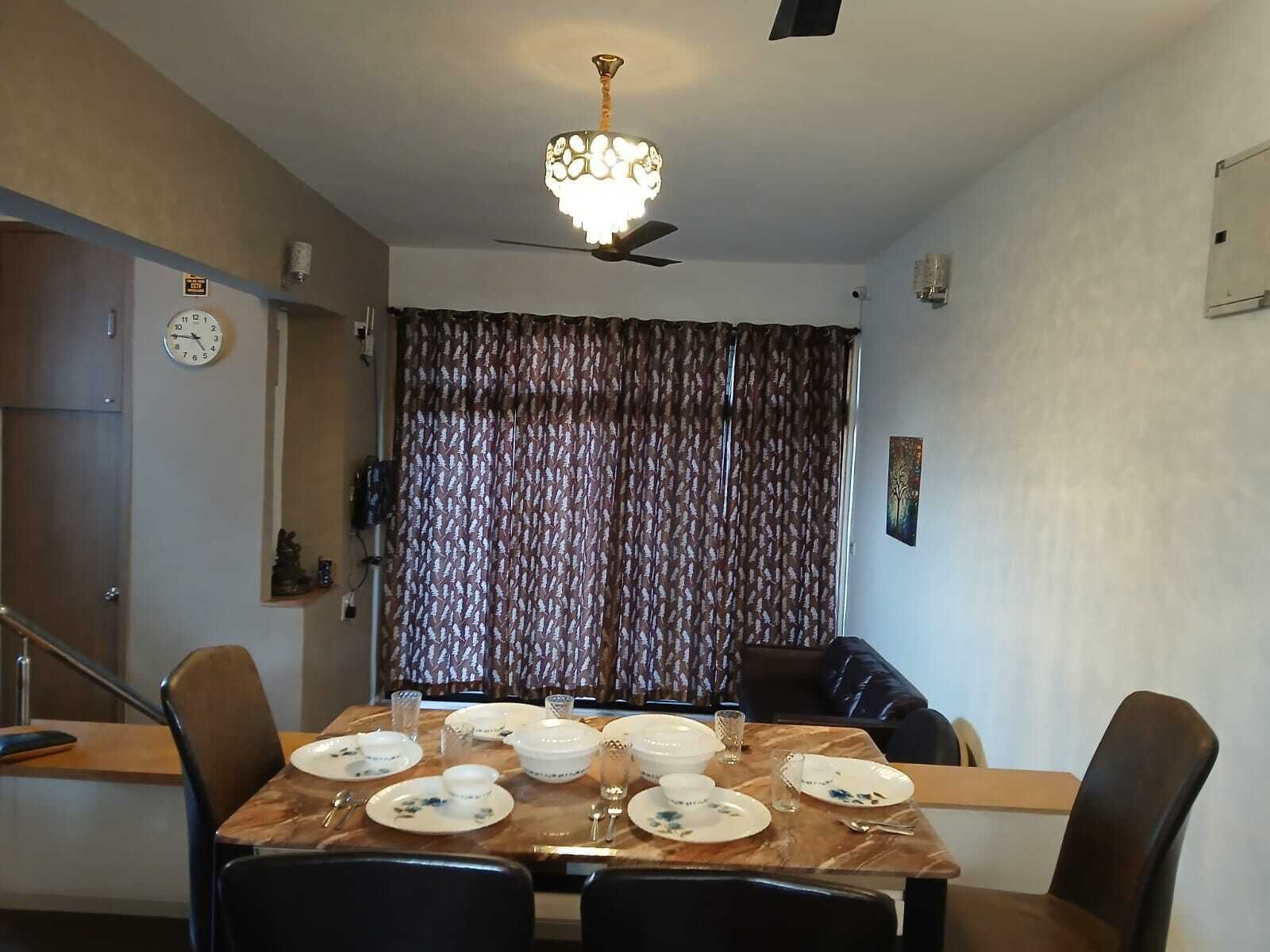 Un comedor con una mesa dispuesta para cuatro personas, un ventilador de techo y un reloj en la pared.