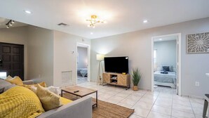 A modern living room with a sofa, TV, and a small table. There are two doors leading to other rooms.