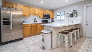 A modern kitchen with wooden cabinets, stainless steel appliances, a white countertop, and a trash can.