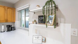 A modern kitchen with wooden cabinets, a coffee machine, a white countertop, a sign indicating a WiFi password, and a hanging plant.
