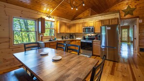 A wooden cabin kitchen with a dining table, chairs, a refrigerator, a microwave, and a stove. - Big Oak Cabin (Hocking Hills area) (Rockbridge)