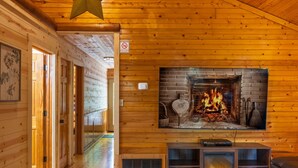 A wooden cabin interior with a fireplace, a television mounted above it, and a hallway leading to another room. - Big Oak Cabin (Hocking Hills area) (Rockbridge)