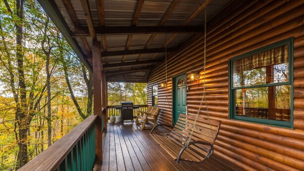 A wooden cabin with a porch, a swing, and a view of autumn trees. - Big Oak Cabin (Hocking Hills area) (Rockbridge)