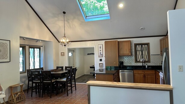 A spacious kitchen with a dining area, a chandelier, and a skylight.