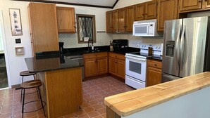 A kitchen with wooden cabinets, a stainless steel refrigerator, a microwave, an oven, and a bar stool.