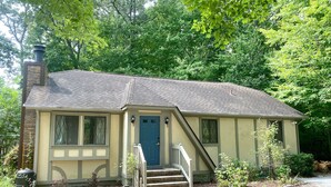 A single-story house with a front porch, a chimney, and a blue door.