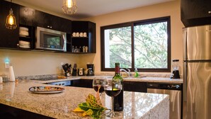 Una cocina con encimeras de granito, electrodomésticos de acero inoxidable y un ventanal con vistas a árboles.