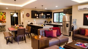 Una cocina moderna con refrigerador, microondas y pileta. Hay un comedor con mesa y sillas. La sala de estar tiene un sofá y una mesita.