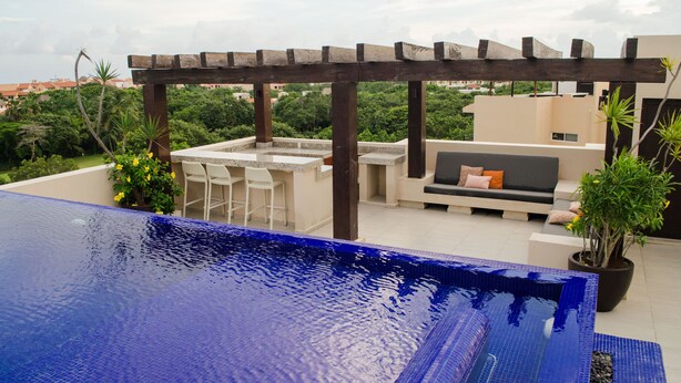 Un área de piscina en la azotea con una pérgola, asientos al aire libre y vistas de la ciudad.