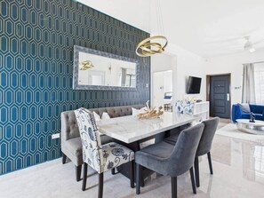 Un espace de salle à manger moderne avec une table en marbre, des chaises à revêtement gris et un mur orné de motifs.
