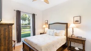 A bedroom with a large bed, two bedside tables with lamps, a wooden dresser, and a view of a green lawn through a window. - Spacious and Private Pool Home- Pet Friendly (Naples)
