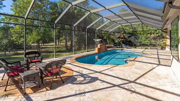 A covered outdoor swimming pool with a patio area, surrounded by chairs and a pergola. - Spacious and Private Pool Home- Pet Friendly (Naples)