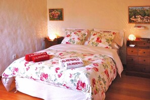 A neatly made bed with floral bedding and a red pillow with text. - Casa Tres Almendros (Vega de San Mateo)