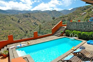 A swimming pool with a stone wall and a wooden deck with lounge chairs. - Casa Tres Almendros (Vega de San Mateo)