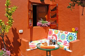 A vibrant outdoor seating area with a colorful sofa, a small table with a teapot, and a window with a view of a tree and flowers. - Casa Tres Almendros (Vega de San Mateo)