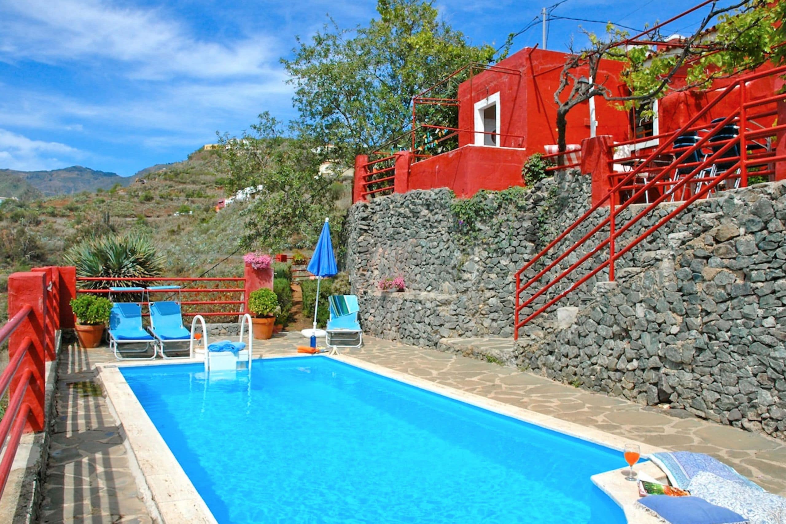 A swimming pool with blue water, surrounded by stone walls and red railings.