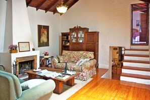Ein Wohnzimmer mit Kamin, einem blumigen Sofa, einem Holzkabinett und einer Treppe.