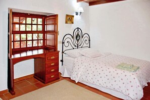 Ein Schlafzimmer mit einem Holztisch, einem Bett mit floralem Bettzeug, einer Wandlampe und einem kleinen Bilderrahmen.