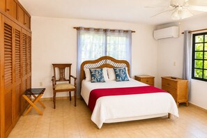 Ein Schlafzimmer mit Bett, Sessel, Nachttisch, Kleiderschrank und einem Fenster mit Vorhängen.