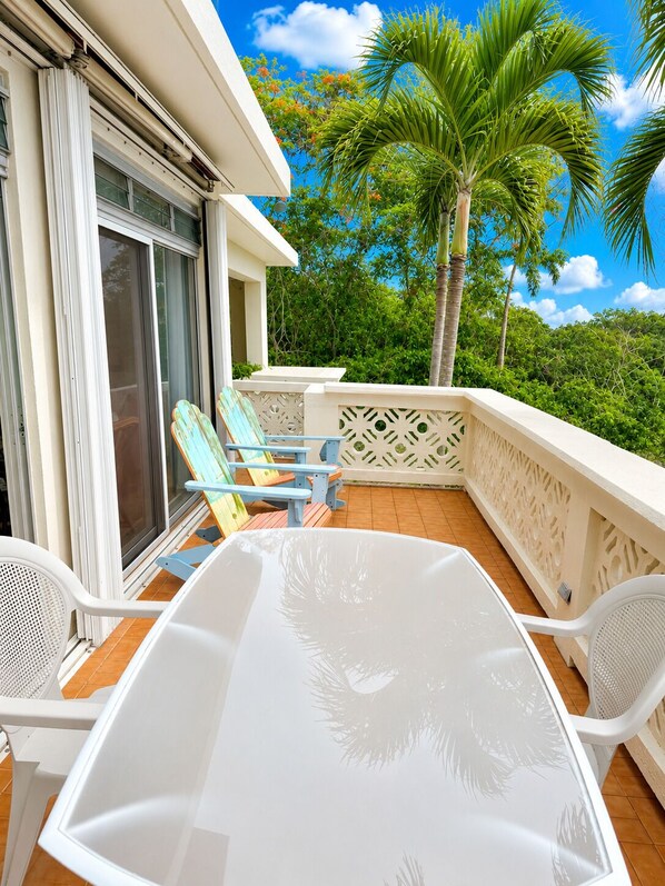 A balcony with a white table and chairs, a palm tree, and a view of greenery.