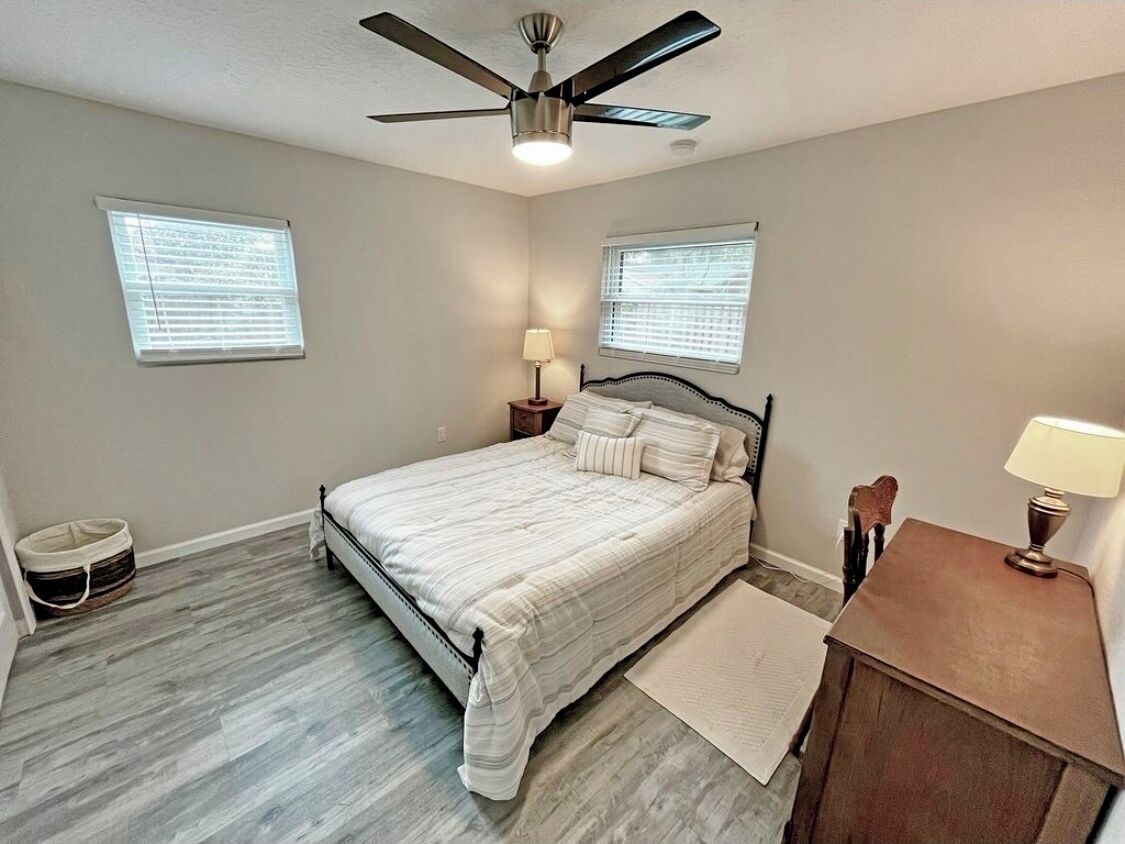 A bedroom with a bed, a ceiling fan, two bedside tables with lamps, and a window with blinds.