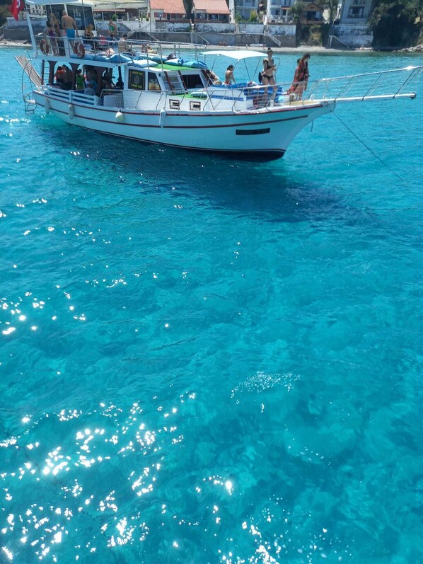 Un bote con pasajeros, agua turquesa cristalina y edificios al fondo.