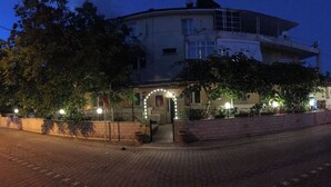 A building with a curved facade, a brick pathway, and a small garden area with potted plants. - benjy motel pansiyon (Akcay)