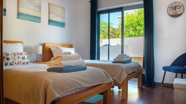 A hotel room with two beds, a bench, a chair, and a view of the outdoors. - Perfectly located apartment. Close to the town and the beaches. (Fuseta)