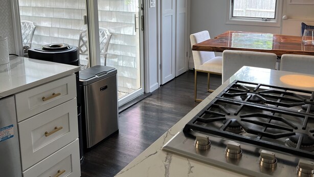 Una cucina moderna con piano cottura a gas, mobili bianchi e una porta scorrevole in vetro che dà su un patio.