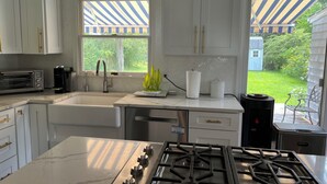 Una cucina moderna con mobili bianchi, fornello a gas, lavandino e finestra vista giardino.