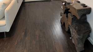Un soggiorno moderno con un divano bianco, un tavolino in legno e un grande specchio. Si notano quadri appesi al muro e una porta con una finestra.