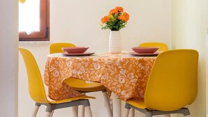 Et spiseområde med et bord dækket til fire personer, gule stole, en hvid vase med orange blomster og et grønt ur på væggen.