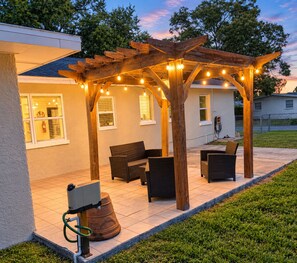 A covered outdoor seating area with string lights, a fire extinguisher, and a hose on the ground.