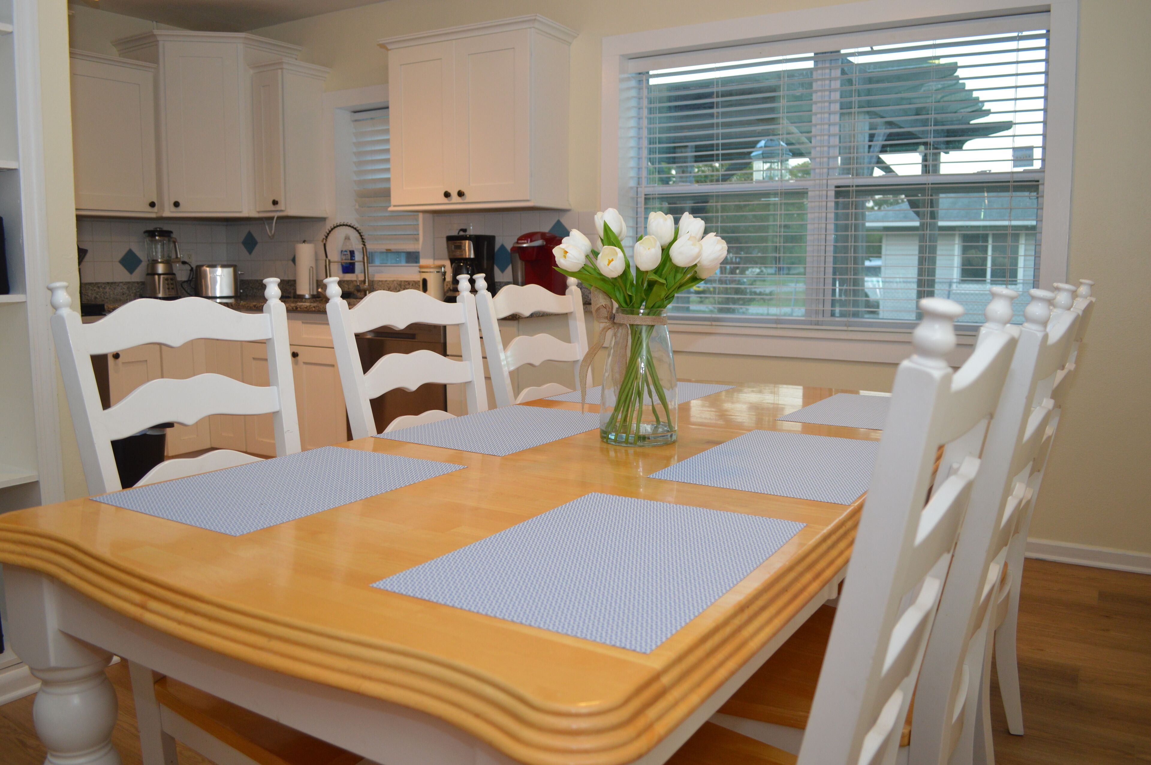 A dining table with a vase of white flowers, surrounded by white chairs.