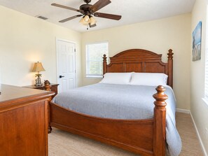 A bedroom with a wooden bed, a ceiling fan, a window with blinds, and a door.