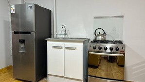 A compact kitchen with a stainless steel refrigerator, a small white cabinet, and a gas stove. - Comfortable/Cozy SKY HOUSE CUSCO (CUSCO)