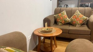 A living room with a brown sofa, two floral pillows, a small wooden table with a woven placemat, and a patterned throw on a brown armchair. - Comfortable/Cozy SKY HOUSE CUSCO (CUSCO)