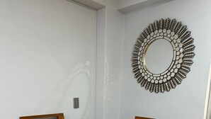 A dining area with a glass table, two wooden chairs, a colorful woven placemat, and a decorative mirror on the wall. - Comfortable/Cozy SKY HOUSE CUSCO (CUSCO)
