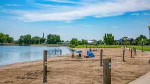 Une zone de plage sablonneuse avec un lac, des tables de pique-nique et une tente.