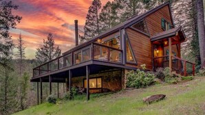 A modern cabin with a wooden exterior, a deck, and a stone foundation. - Private Lakefront Sanctuary | Cedar Hot Tub + 6 Acres, No Neighbors (Nevada City)