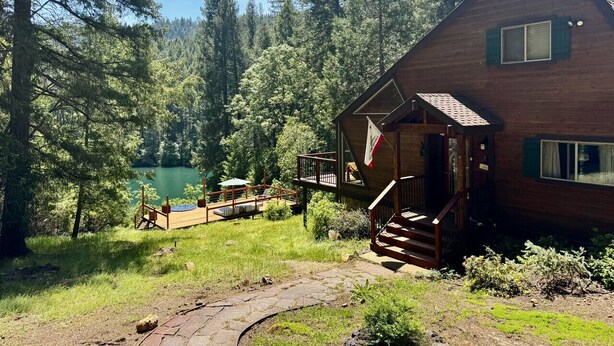 A cabin with a deck, a small porch, and a view of a lake surrounded by trees. - Private Lakefront Sanctuary | Cedar Hot Tub + 6 Acres, No Neighbors (Nevada City)